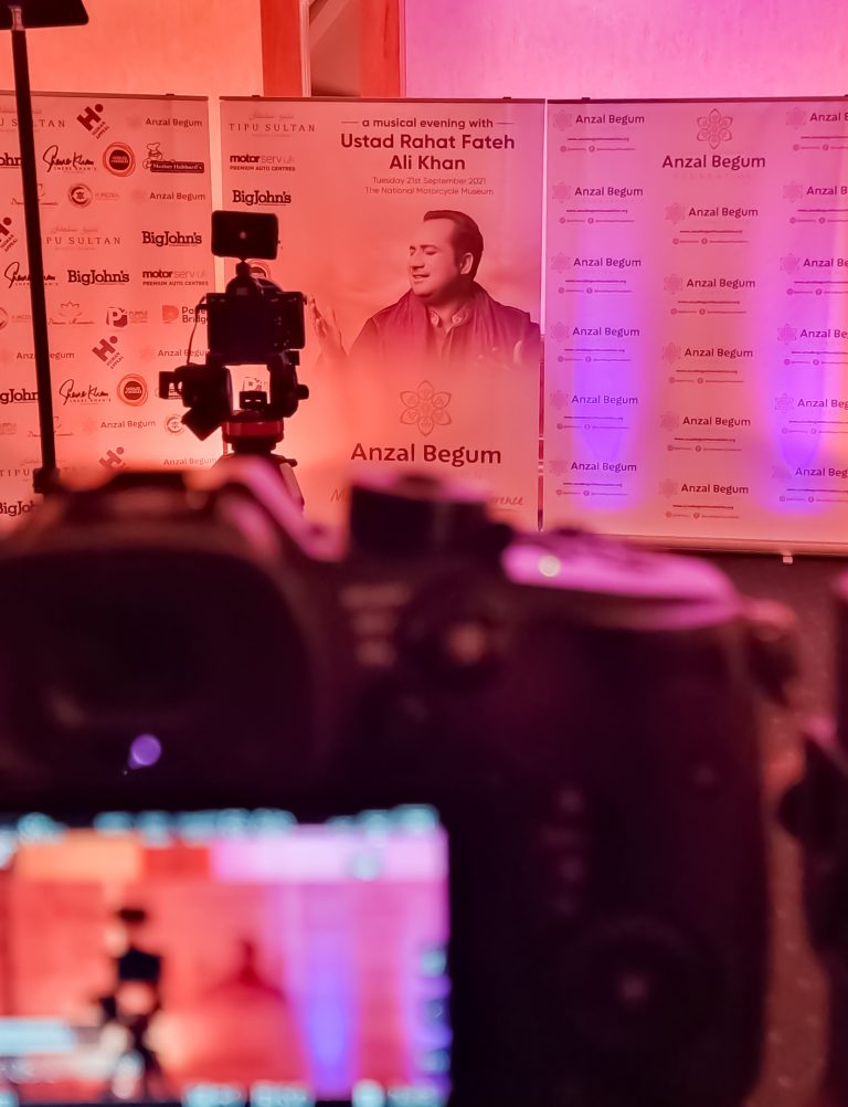 image of a camera facing a photography backdrop setup of an event entitled a musical evening with Ustad Rahat Fateh Ali Khan